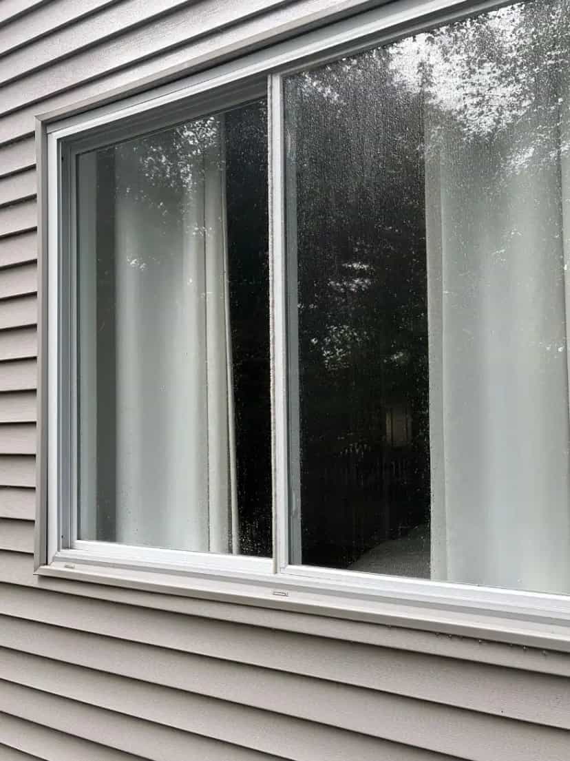 Sliding window on gray vinyl siding with water spots and haze before cleaning
