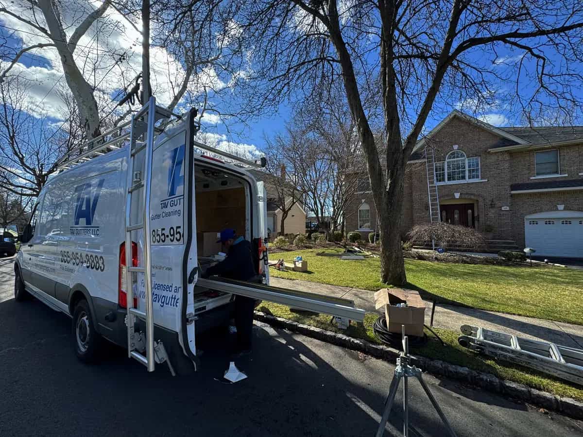 Tav Gutters van with open rear doors and a crew member loading gutter sections in front of a brick house
