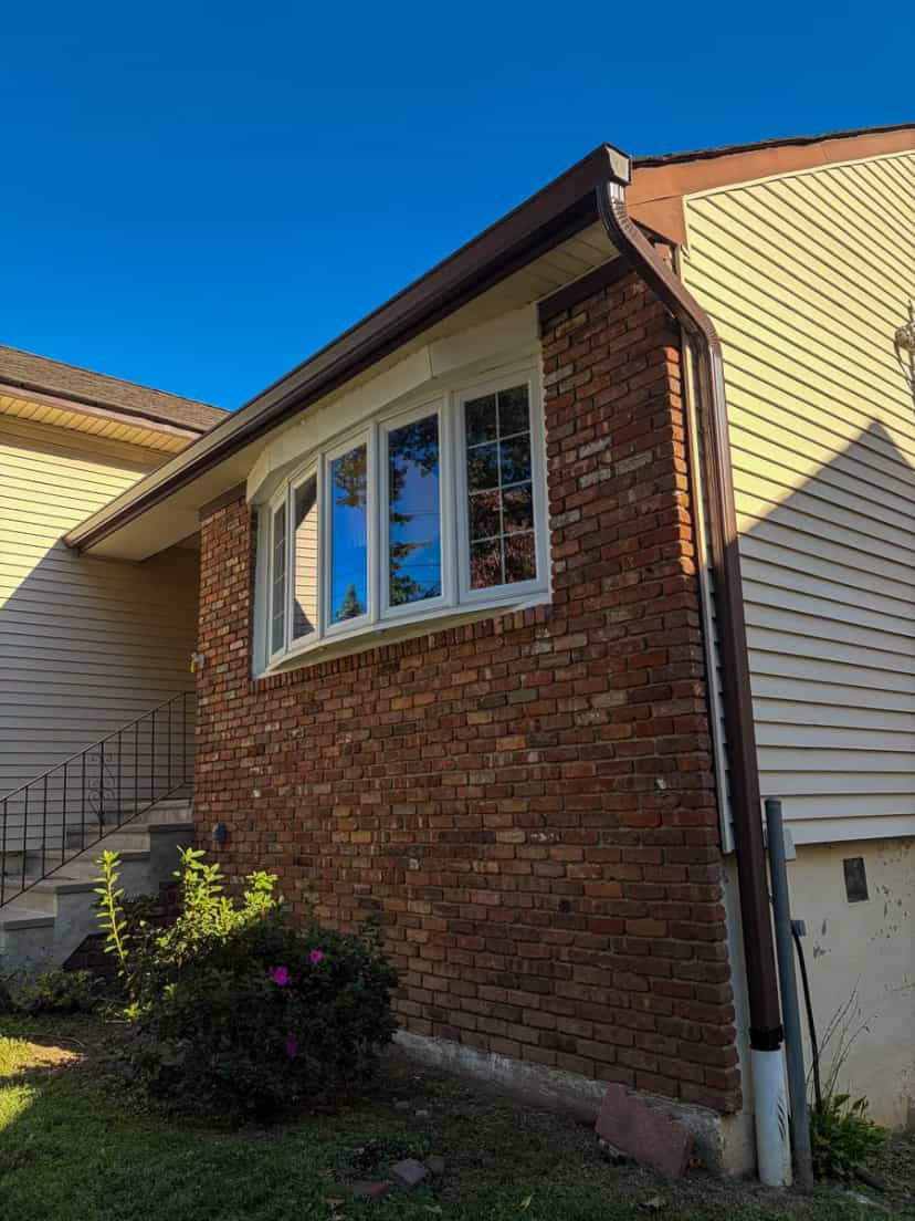 New brown seamless gutter and downspout running down a brick and siding house, blue sky