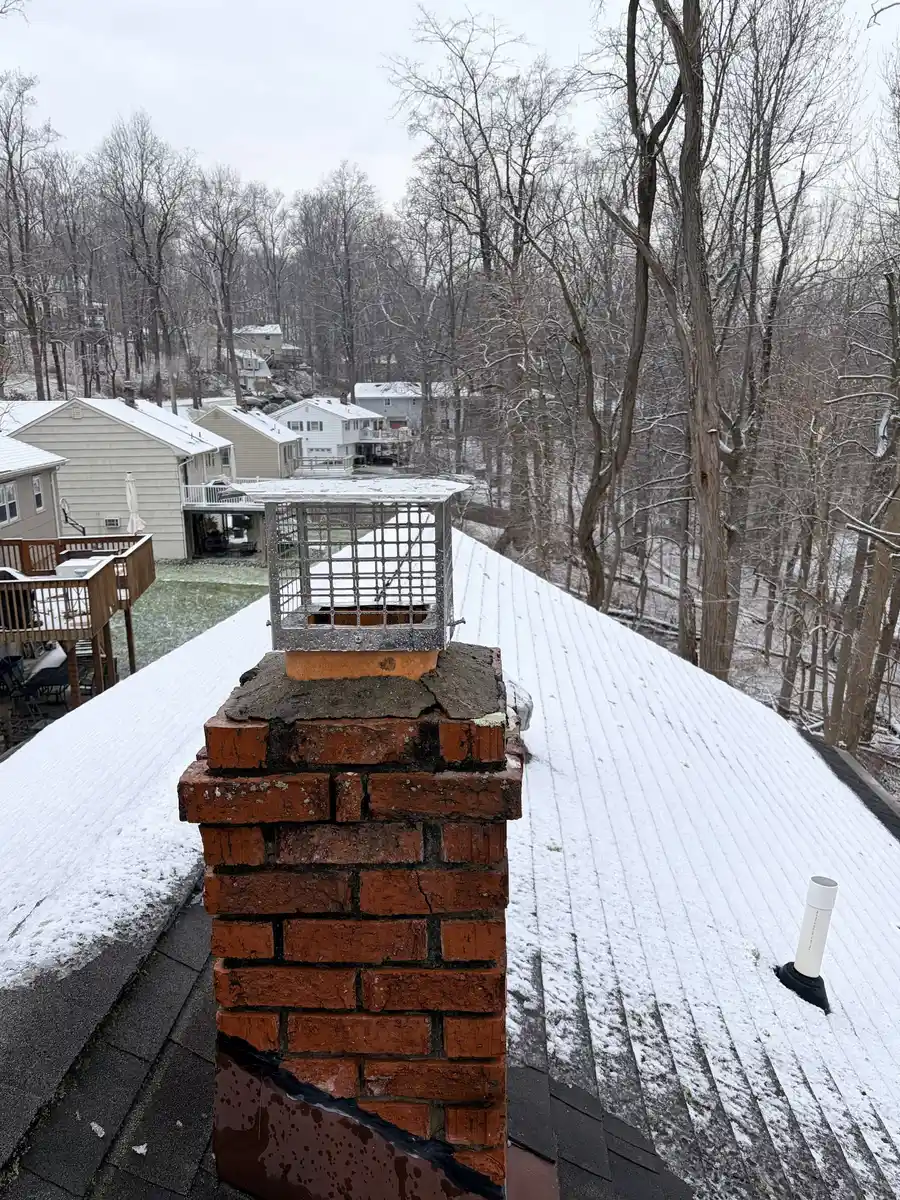 Stainless chimney cap on a brick chimney on a snow-dusted roof