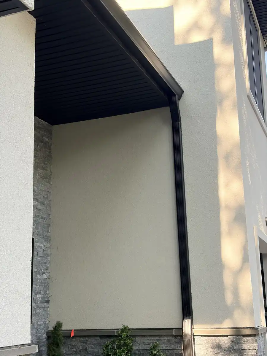 New black downspout running down a stucco wall under a soffit