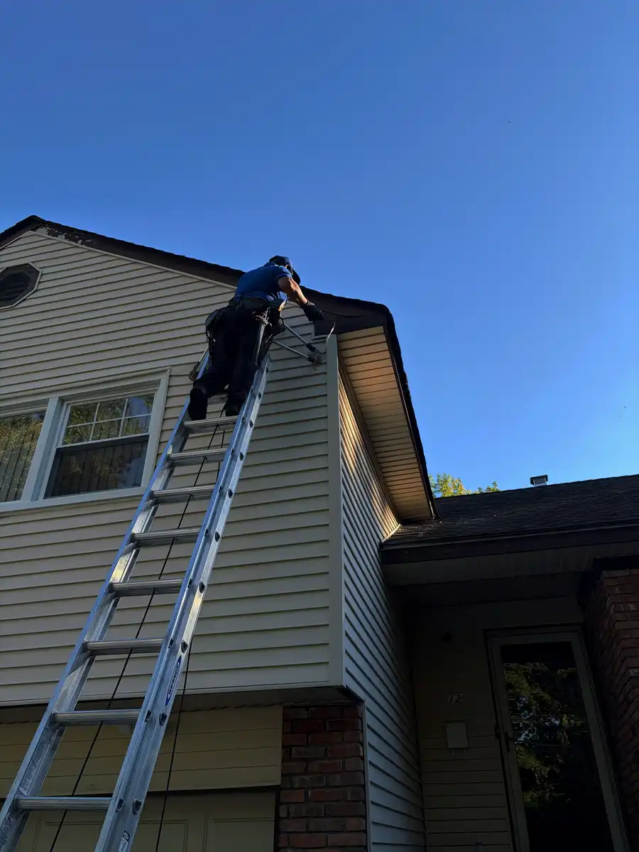 Crew member on a ladder at the roof edge of a two-storey house, blue sky
