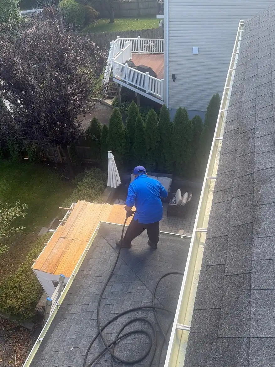 Crew member in a blue shirt hosing a lower roof beside a gutter, seen from above